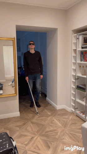 a man wearing sunglasses and holding a cane in a hallway with imgplay at the bottom