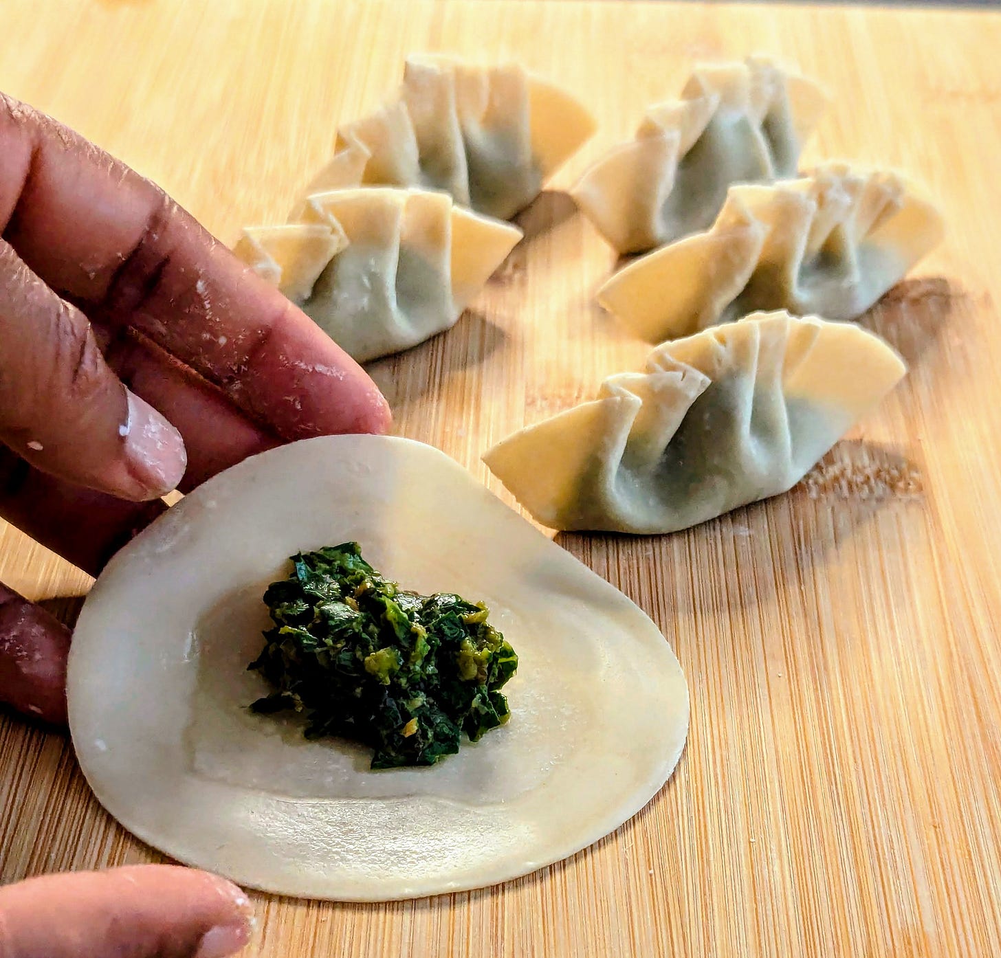 Hand forming a gyoza dumpling on a board with several folded gyoza in the background. 