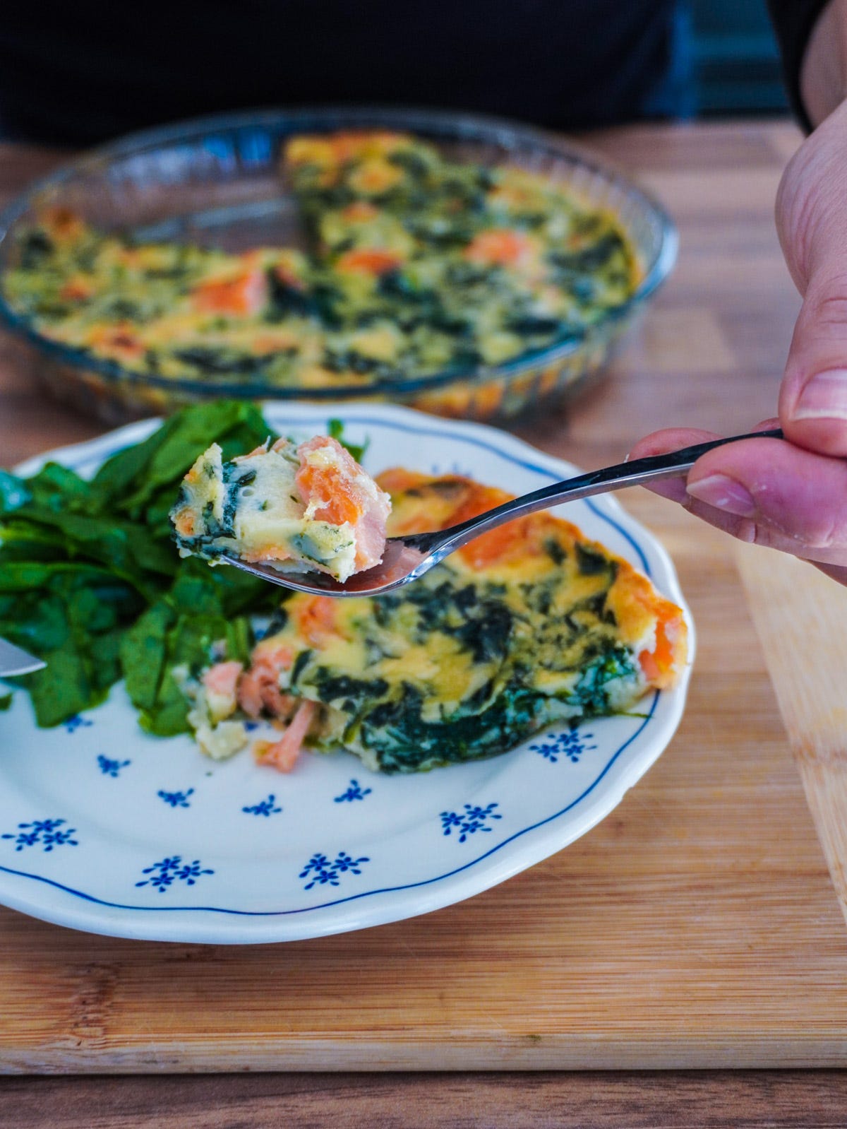 une part de quiche sans pâte epinard saumon tenu dans une fourchette au dessus d'une assiette