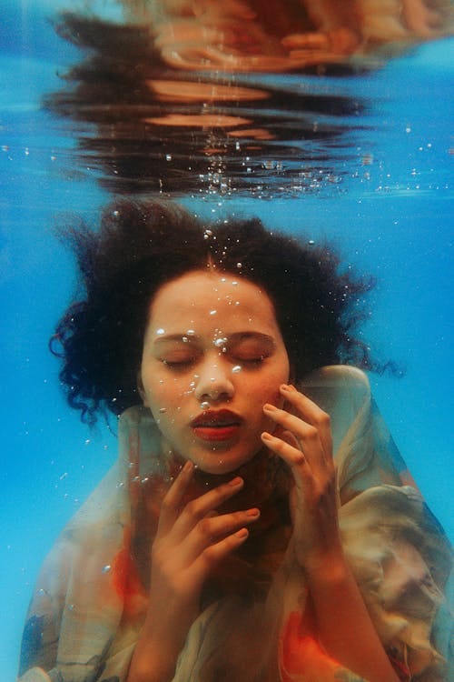 Free Artistic underwater portrait of a woman with eyes closed and hands touching face. Stock Photo