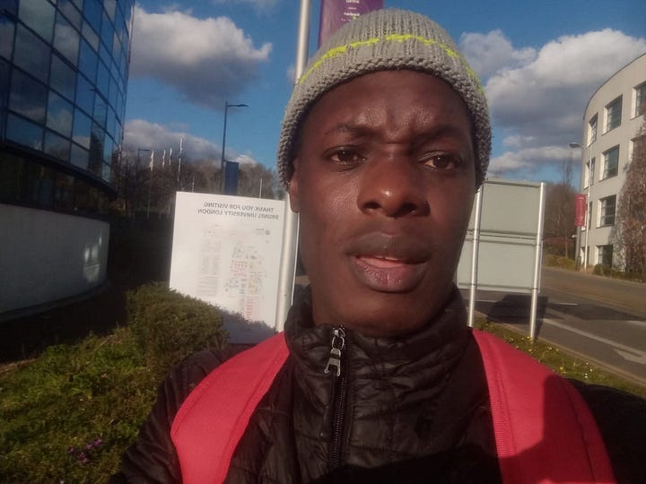 Cristino N. Chávez Jr. (left image): Cristino N. Chávez poses confidently against a solid blue background. He is wearing a white dress shirt with a black tie and has his arms crossed. He has short curly dark hair, a trimmed beard, and a small hoop earring.  Pius Semutumba (right image): Pius Semutumba takes a selfie outdoors near a university campus. He is wearing a gray knit hat, a black jacket, and a red backpack. The sky is partly cloudy, and campus buildings with glass and white walls are visible in the background.