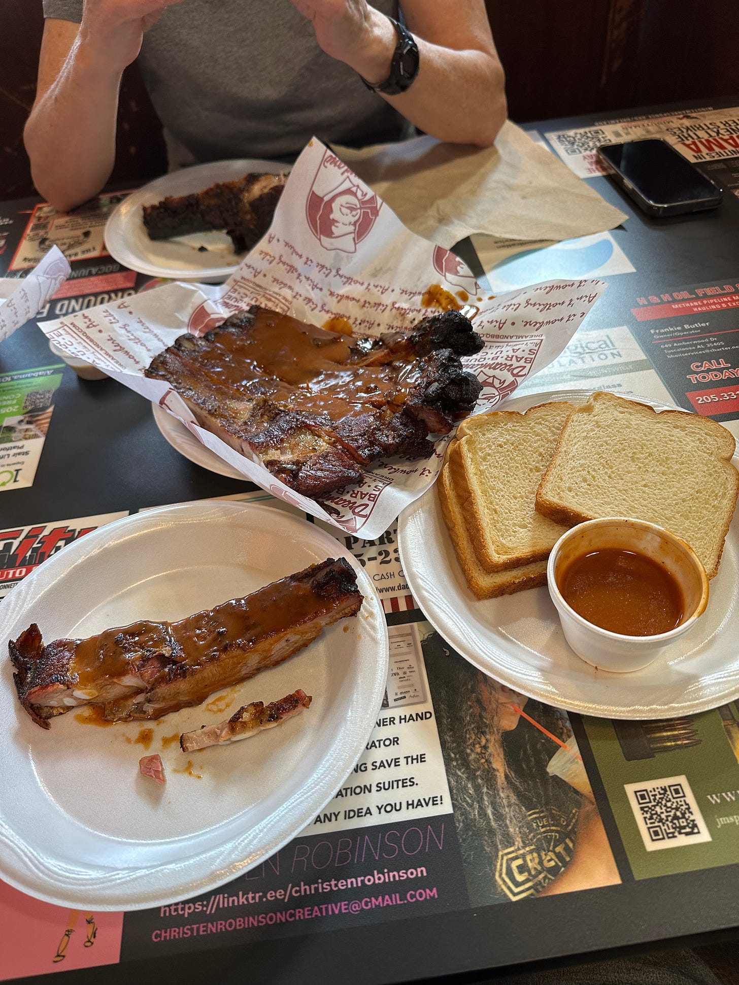Plates with barbeque ribs, sauce, and white bread on a table.