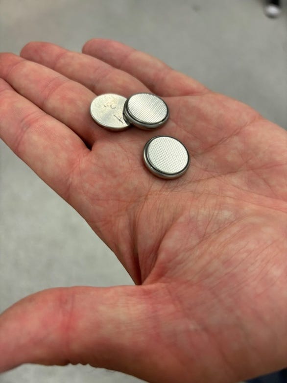 A hand holding several round silver batteries
Description automatically generated