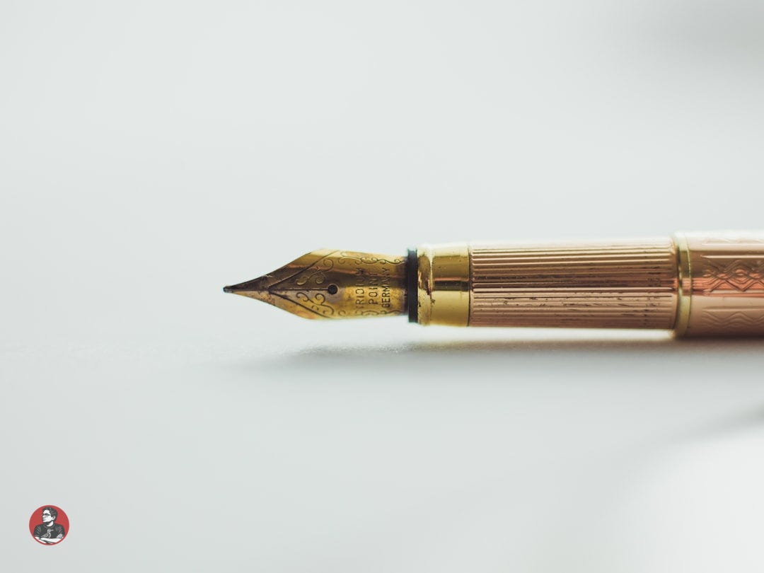 A gold fountain pen with an engraved nib on a white surface