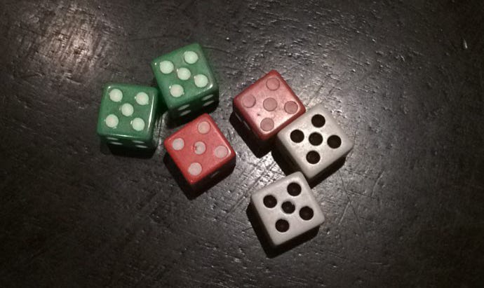 Six die, all showing five, lie atop a black table. It is a close-up shot. Two of the die are green, two are red, two are white. 
