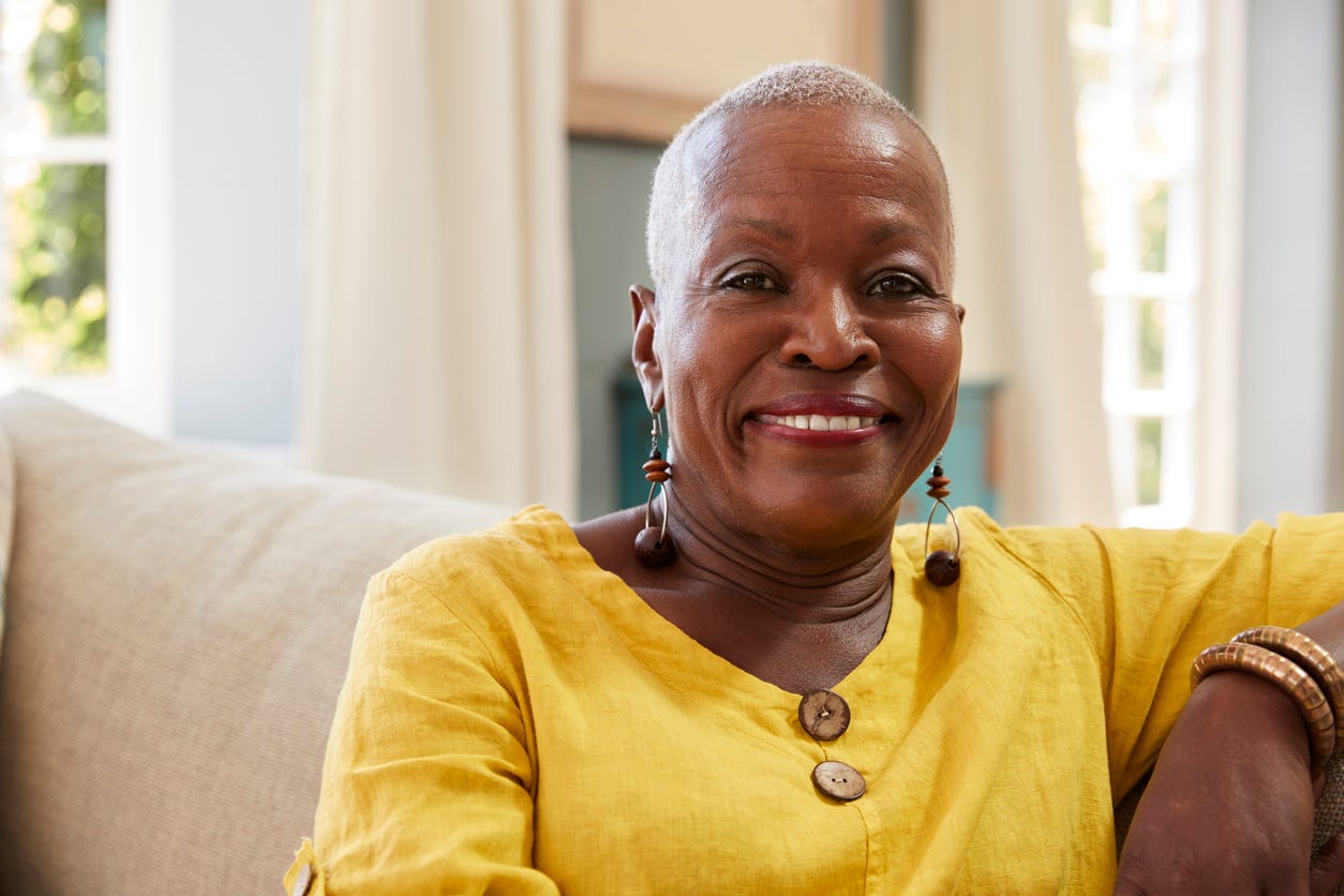 Portrait of older, smiling black woman with fine earrings, bracelett at home.