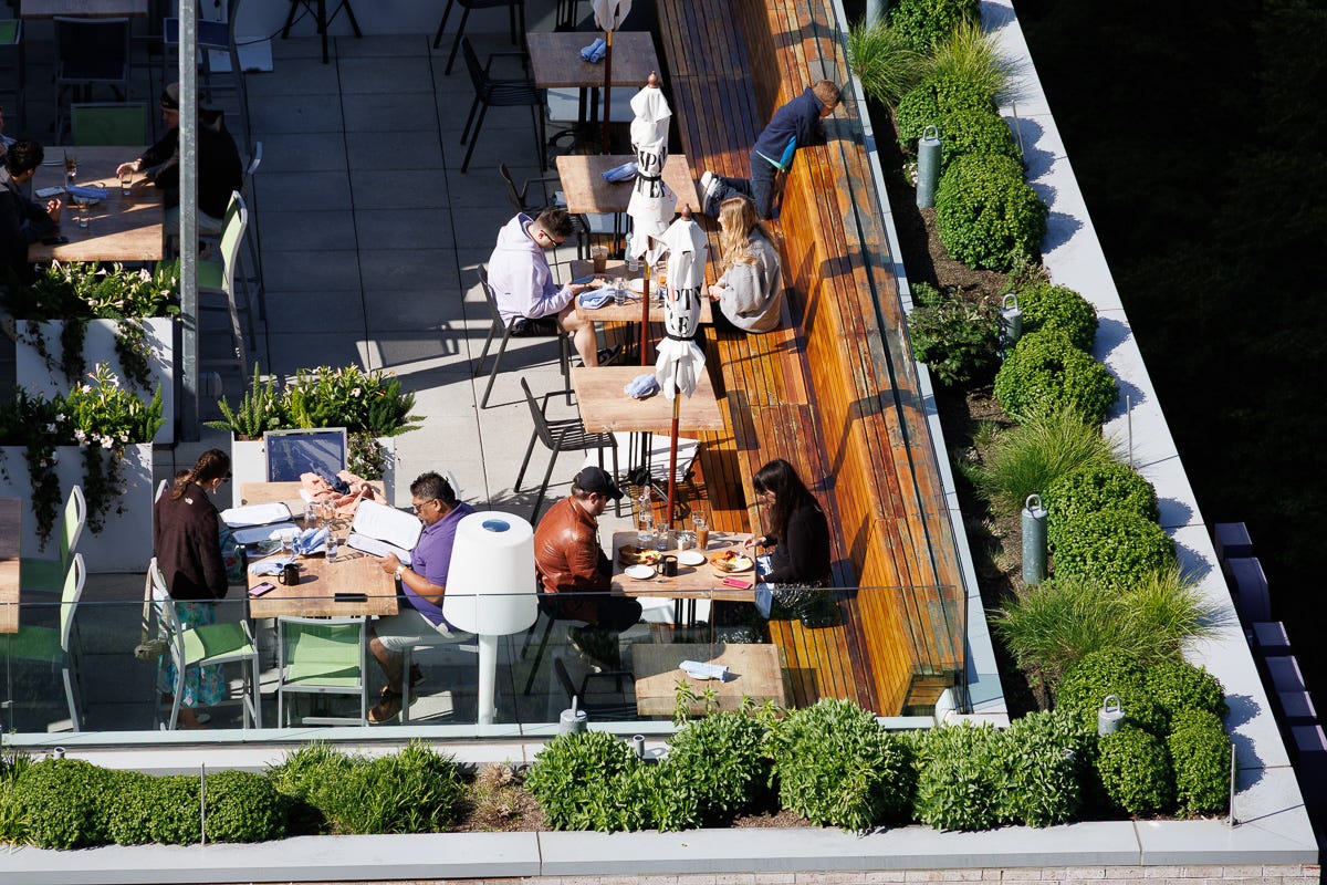 Rooftop dining area with patrons seated under umbrellas during golden hour. Rooftop dining area with patrons seated under umbrellas during golden hour.