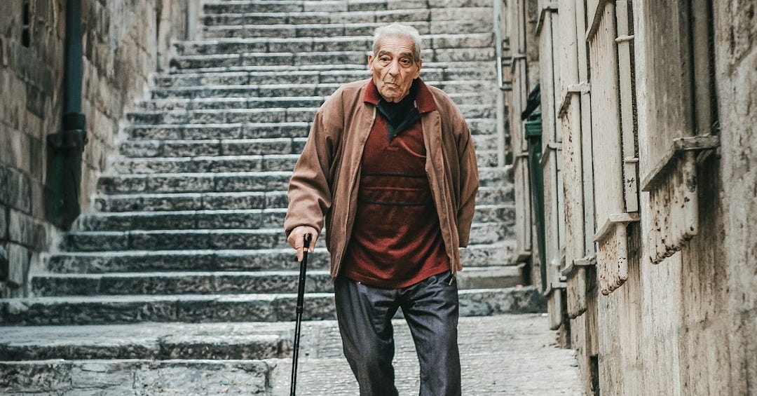 Elderly man with cane walks down stone stairs.