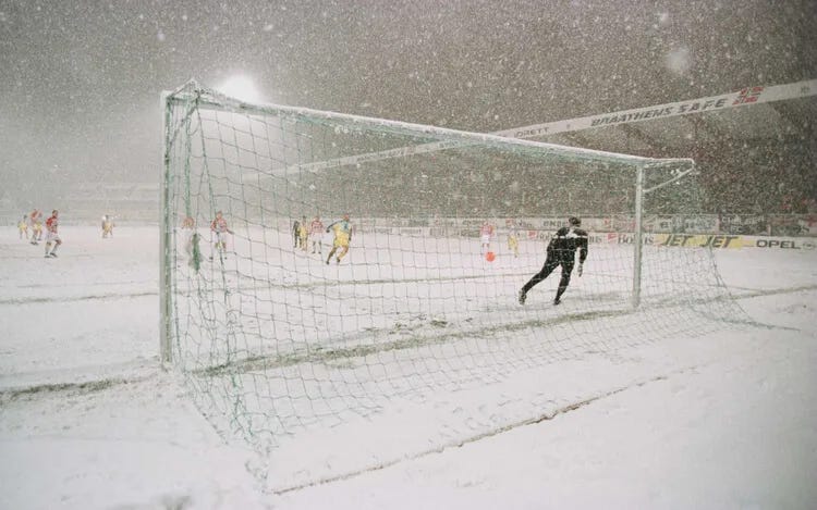 Partido de fútbol durante una nevada, vista desde detrás de la portería