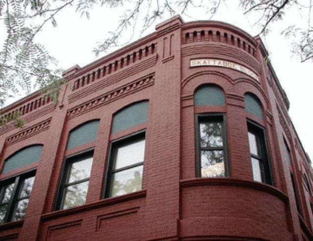 This may contain: an old red brick building with windows and balconies on the top floor, in front of a tree