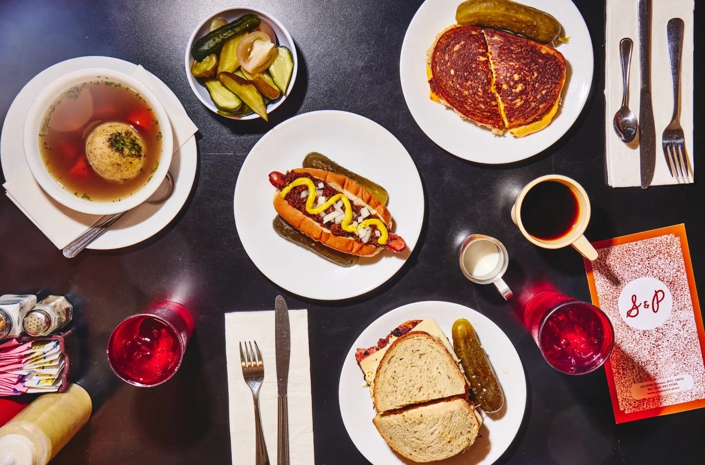 A table of plated food like soups and hot dogs.