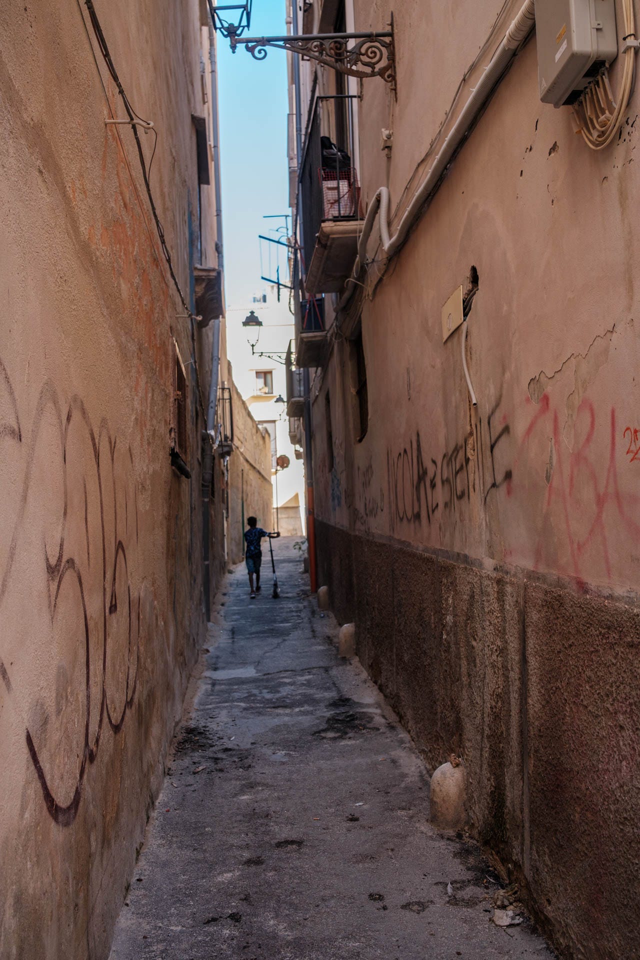 Boy pushing scooter up an alley in Trapani
