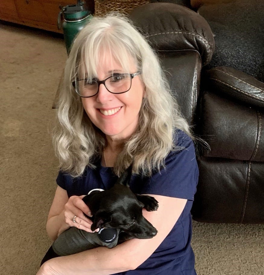 Woman sitting on the floor holding her little black dog in her arms.