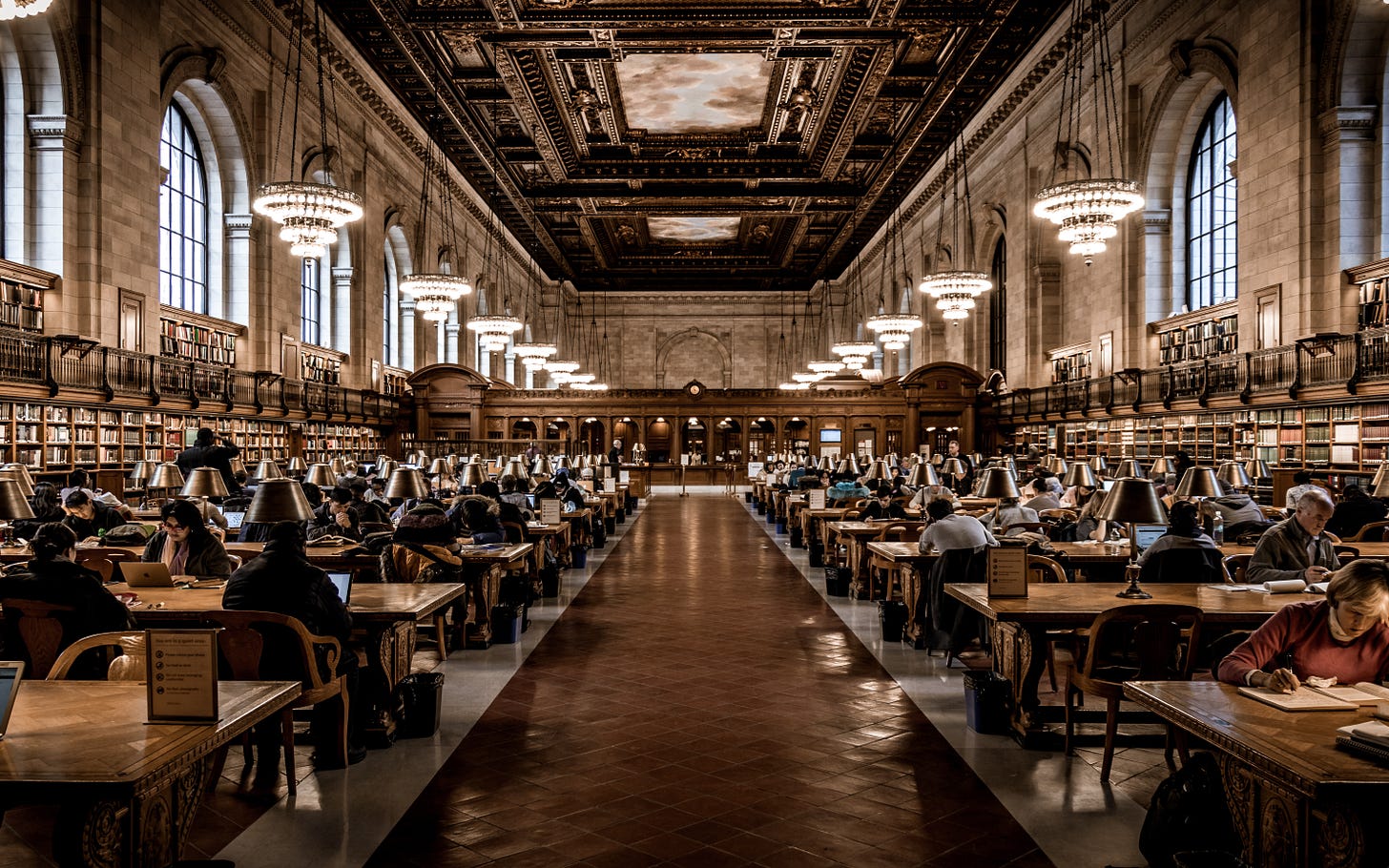 The Rose Main Reading Room at the Stephen A. Schwarzman Building of the New York Public Library, filled with people reading at wooden tables, under chandeliers. The Rose Main Reading Room at the Stephen A. Schwarzman Building of the New York Public Library, filled with people reading at wooden tables, under chandeliers.
