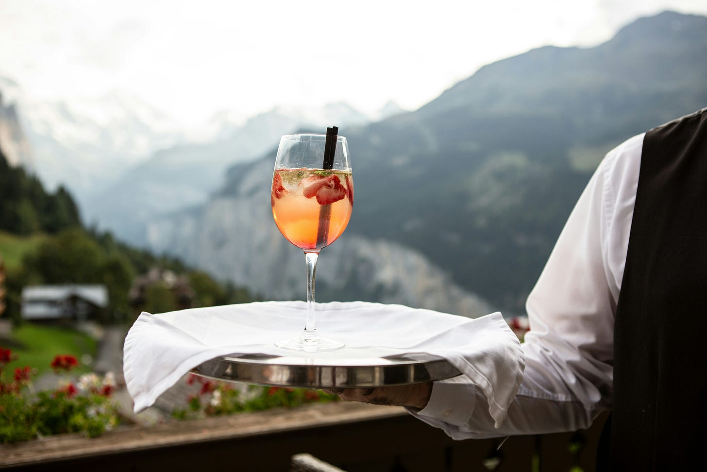 waiter holding a drink on a try with mountains in background