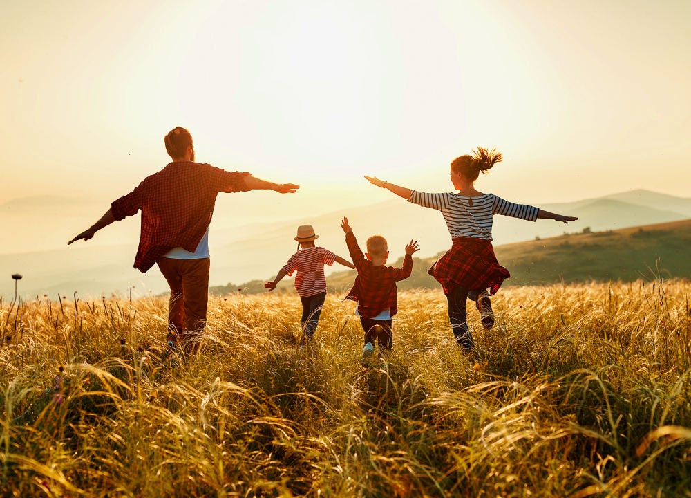 Couple avec deux enfants courant dans un champ vus de dos