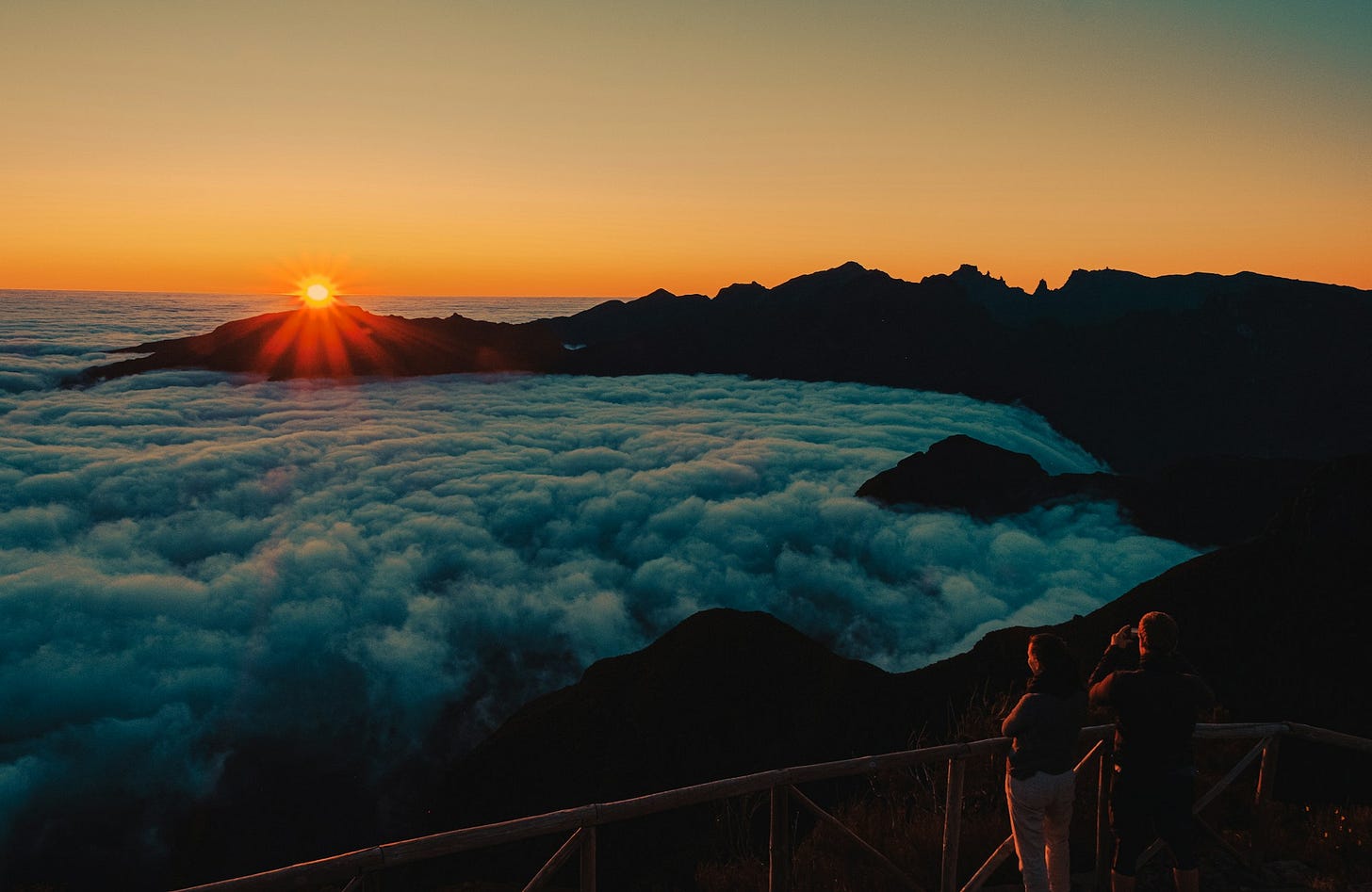 orange sky of early dawn. the sun is just appearing over a pool of thick clouds that extends to the horizon. on the right is the curving silouette of dark hills