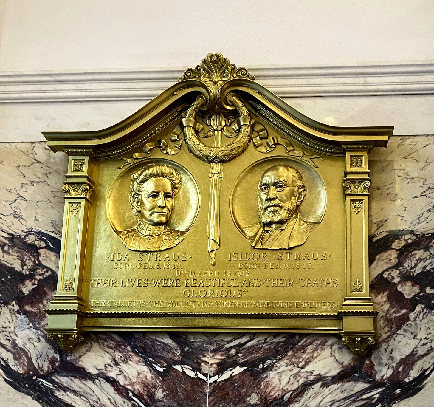 An engraved tablet against the marble wall of Macy's entrance. Below portraits and birth dates and death date of Ida and Isidor Straus, it reads "Their lives were beautiful and their deaths glorious. This tablet is the voluntary token of sorrowing employees." An engraved tablet against the marble wall of Macy's entrance. Below portraits and birth dates and death date of Ida and Isidor Straus, it reads "Their lives were beautiful and their deaths glorious. This tablet is the voluntary token of sorrowing employees."