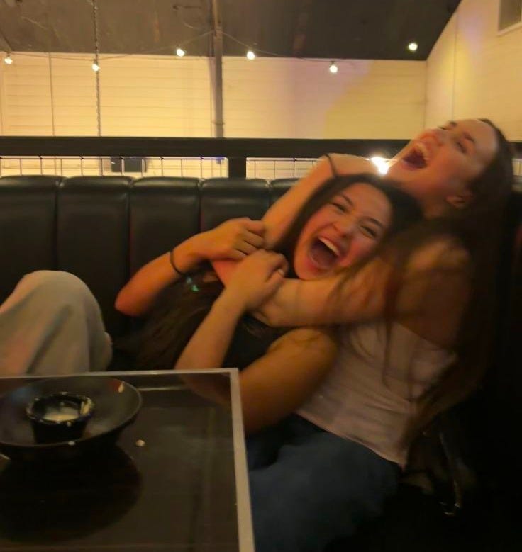 This may contain: two women sitting on a couch with their arms around each other and one woman laughing