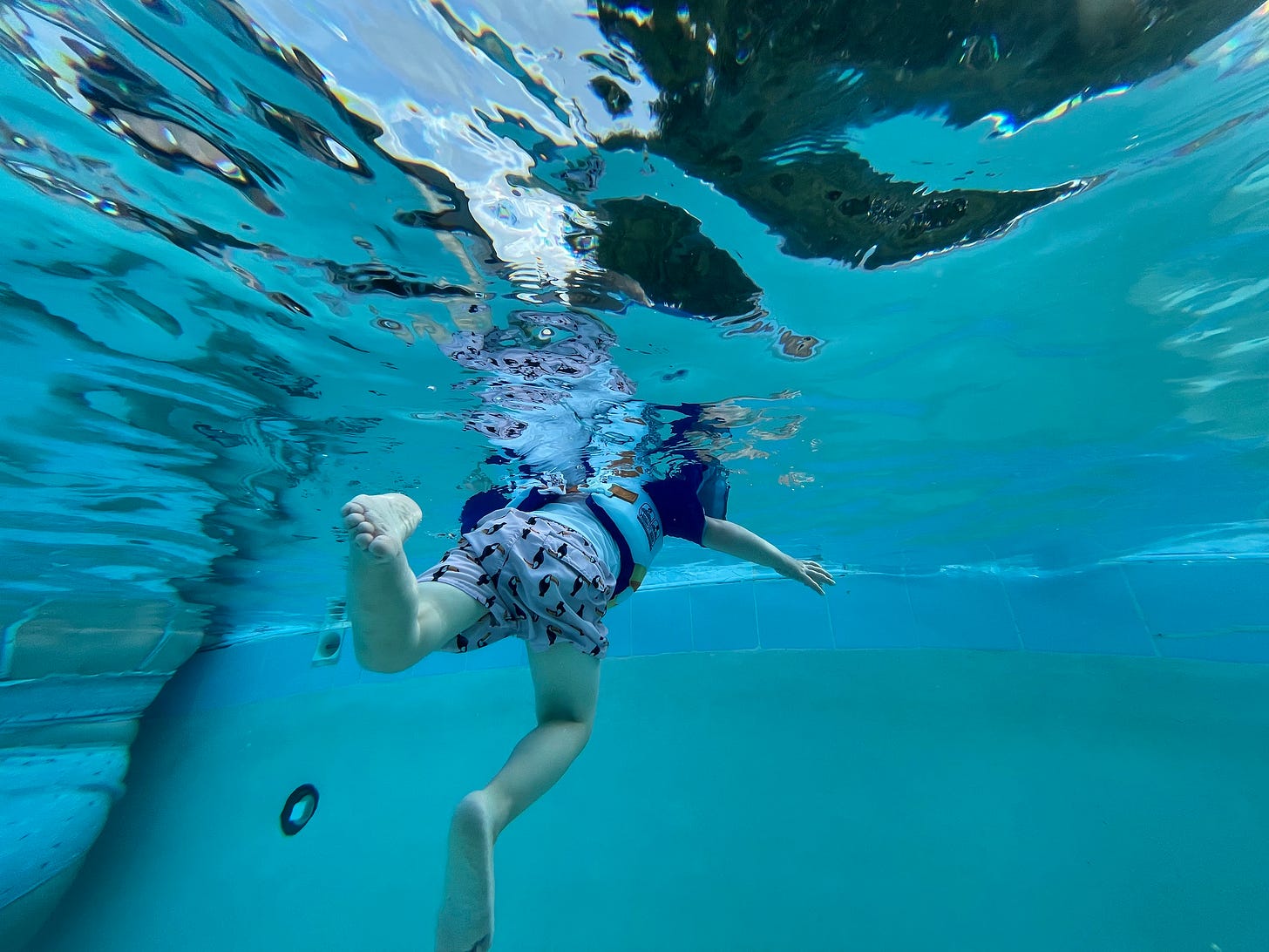 A photo from beneath the water's surface of a young boy swimming.