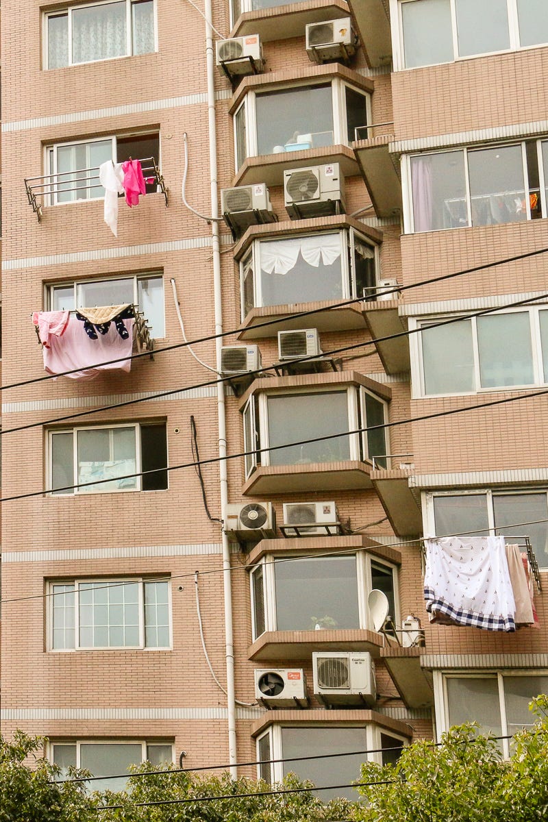 Multiple layers of hanging laundryâ€”sheets, towels, and clothesâ€”cascade from balconies on a densely packed Shanghai apartment facade.