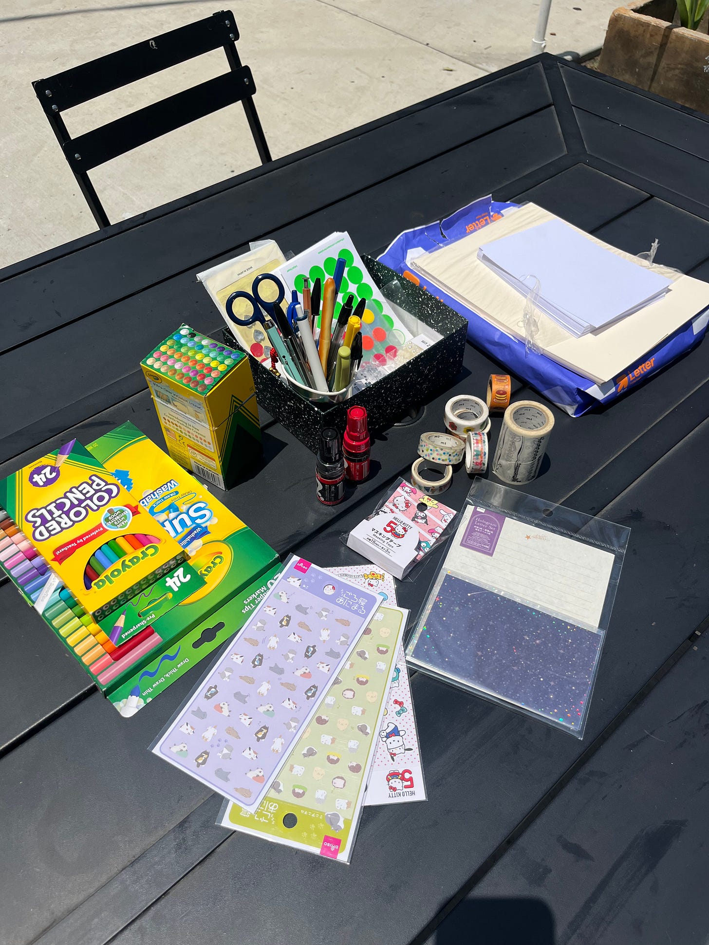 An assortment of letter writing supplies including pens, markers, paper, and sheets of stickers.