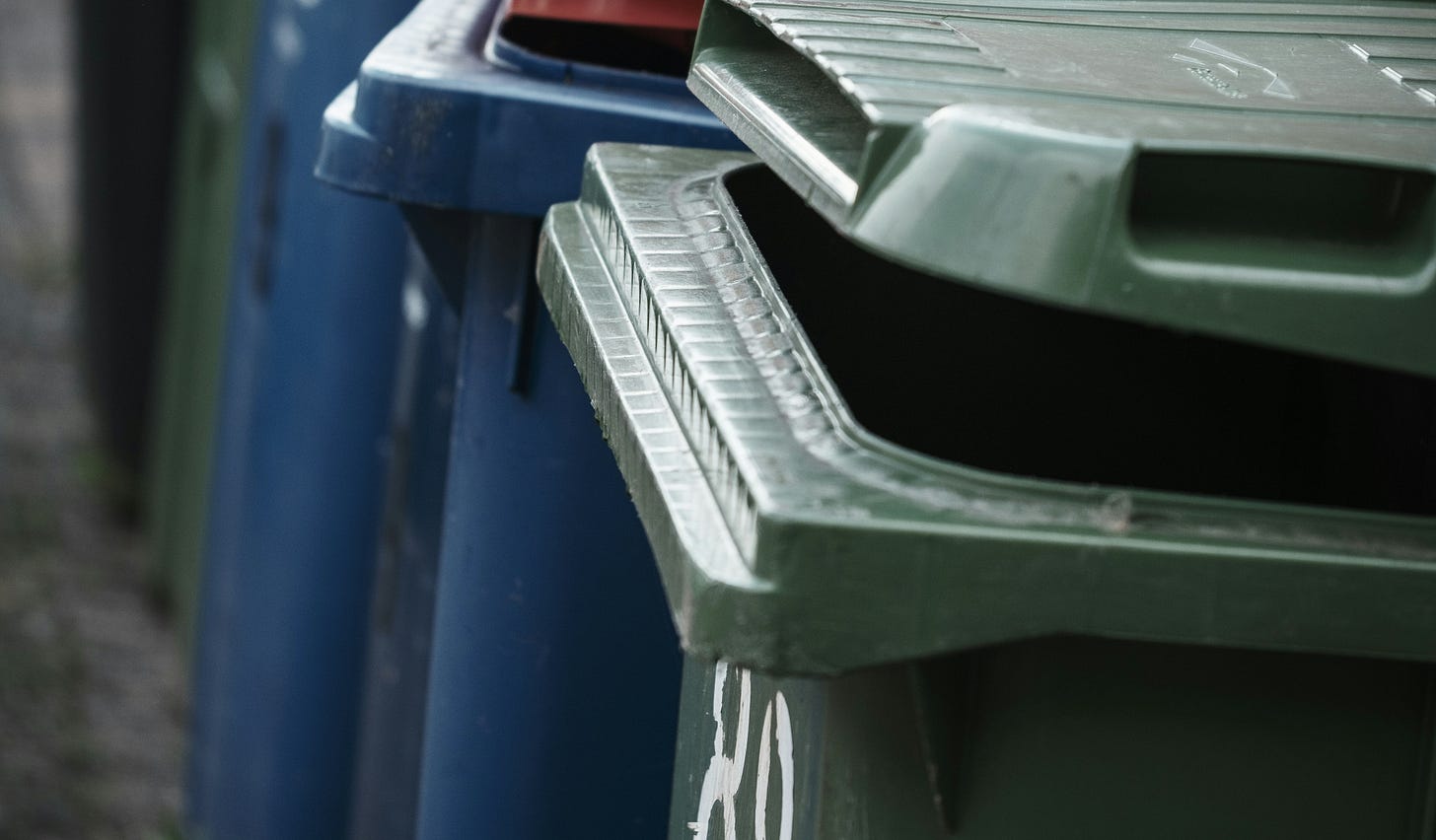 A green bin and two blue bins behind it