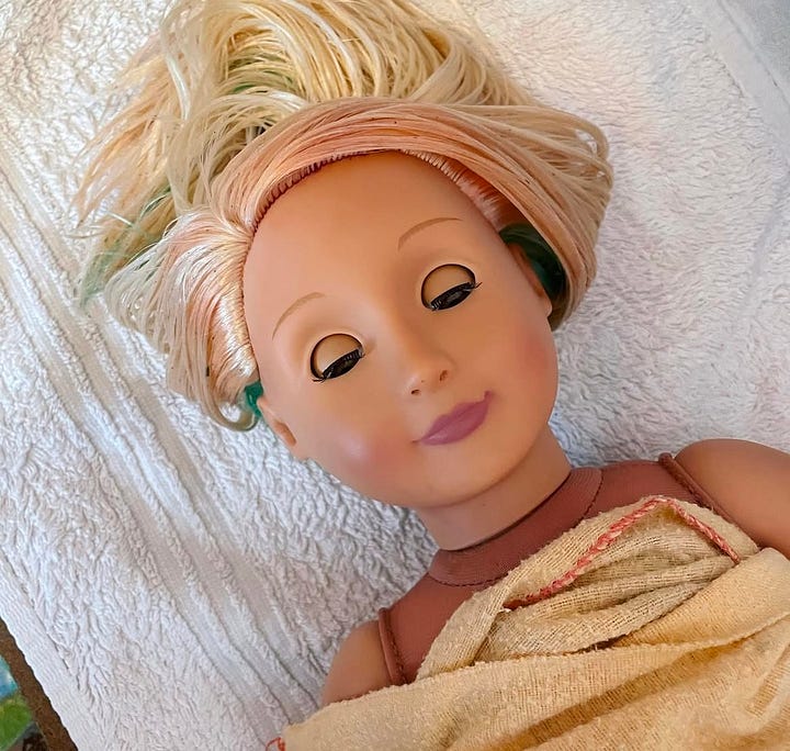A doll covered in construction plaster and leaves with tangled hair. Then lying in a towel with brushed hair. Then clean and dressed in nice clothes sitting next to a teddy bear.