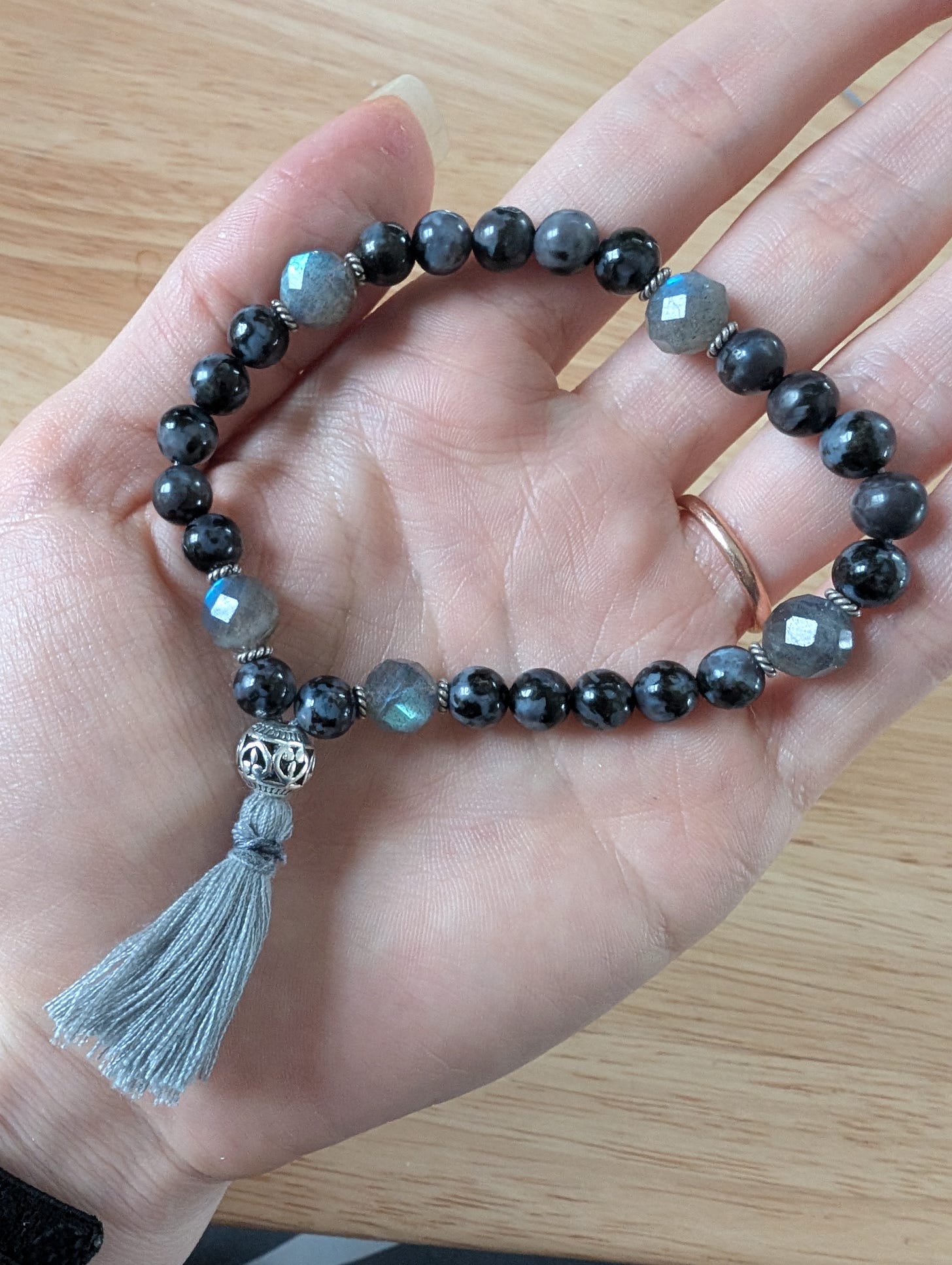 Hand holding a handmade meditation mala with indigo gabbro and labradorite beads, silver spacers, and gray tassel - the Void-Walker's Compass