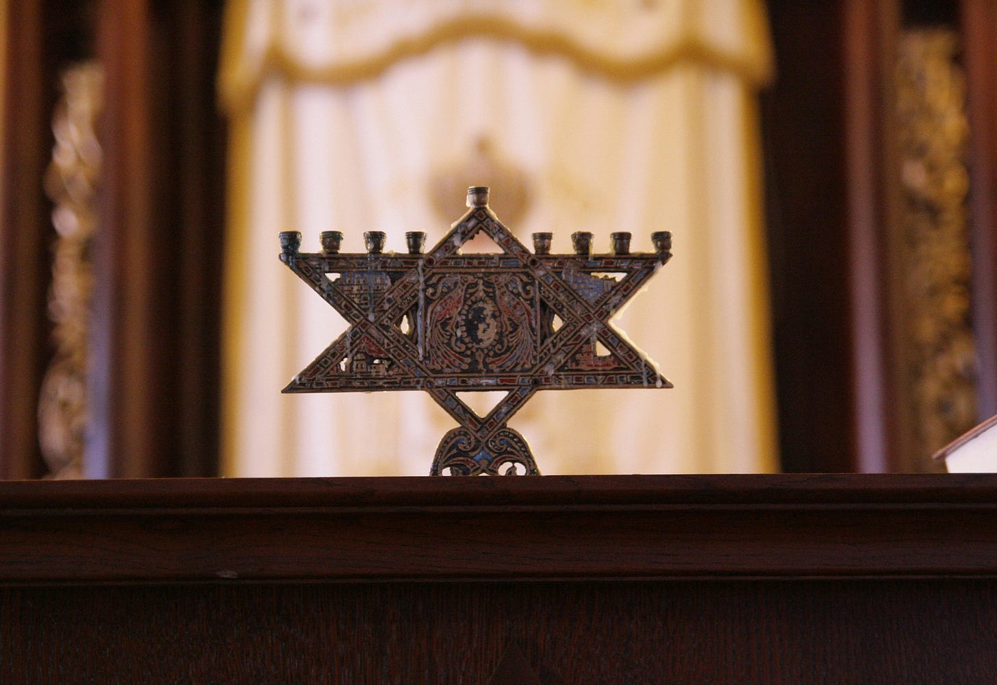 Hanukkah menorah in the shape of a Jewish star, on a wooden table in front of an ark closed with a white curtain with gold trim
