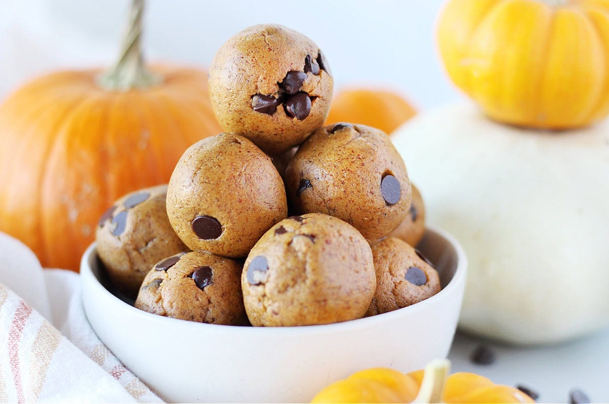 Pumpkin protein balls stacked in a white bowl with pumpkins in the background.