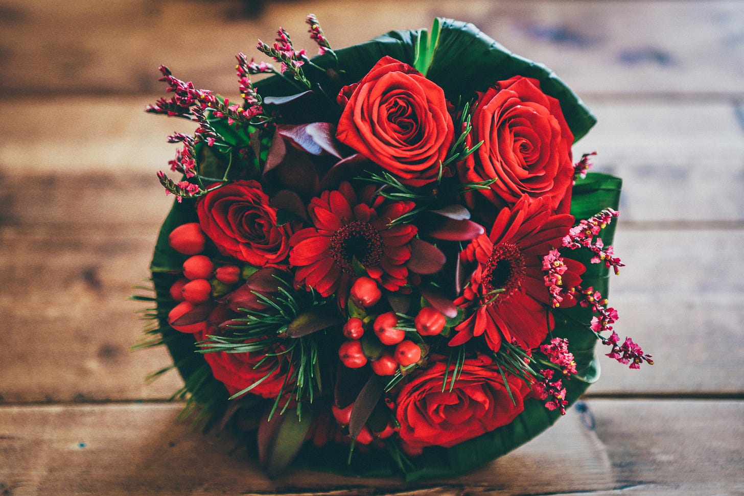 Photo of a bouquet of red flowers lying on a wooden table. Photo of a bouquet of red flowers lying on a wooden table.