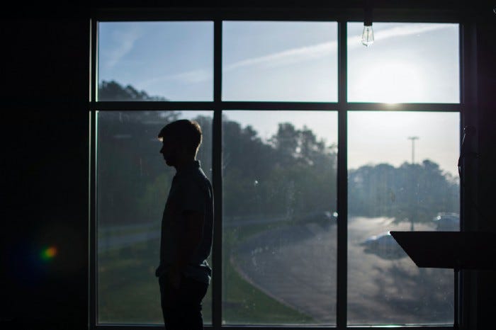 A silhouette of man facing to the left looking introspective while a bright sunny day (and a road) is seen clearly in the background. A silhouette of man facing to the left looking introspective while a bright sunny day (and a road) is seen clearly in the background.