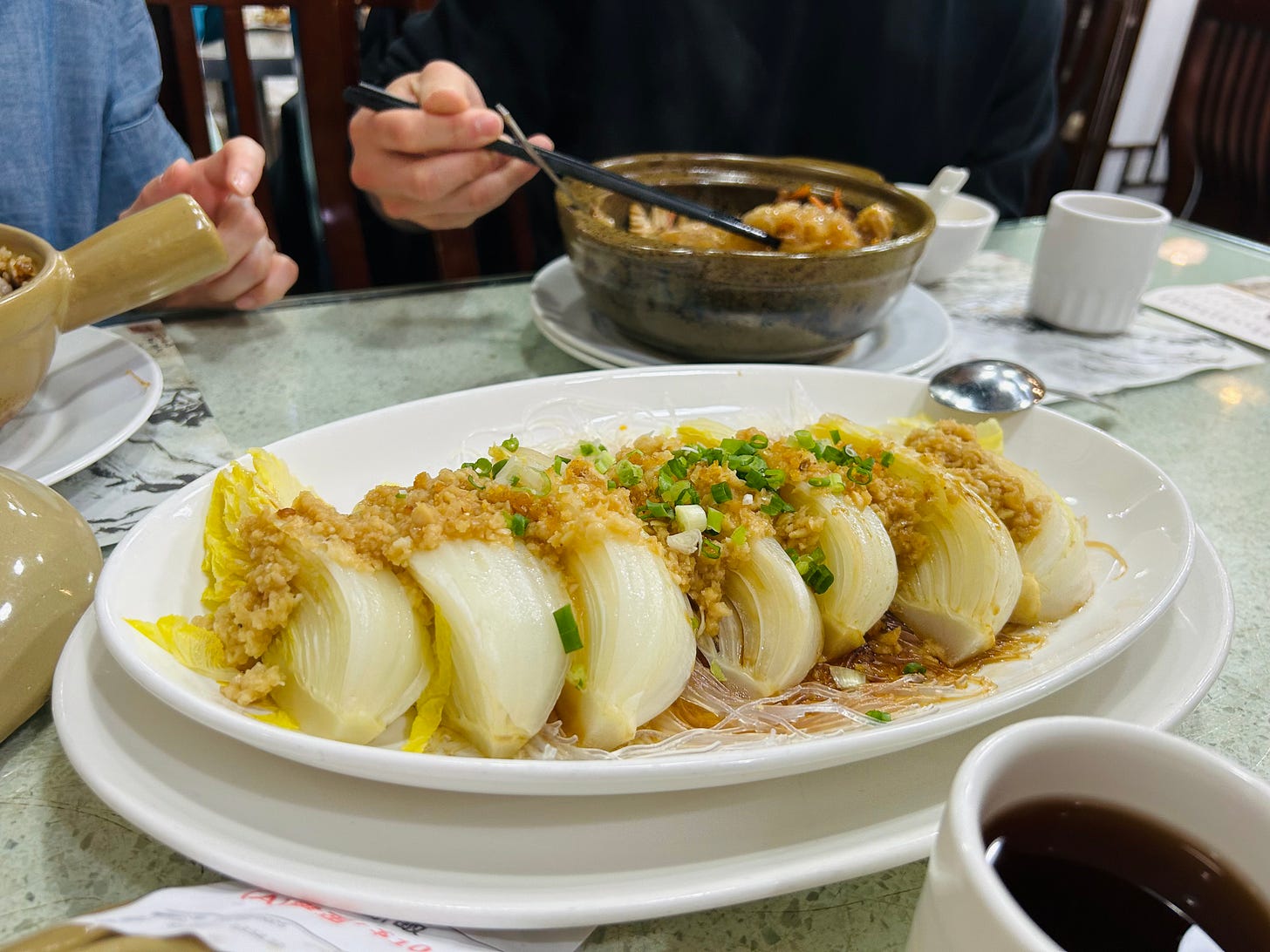 The cabbage and noodle dish on a table at Sheung Hei. Two people are eating on the other side of the table.