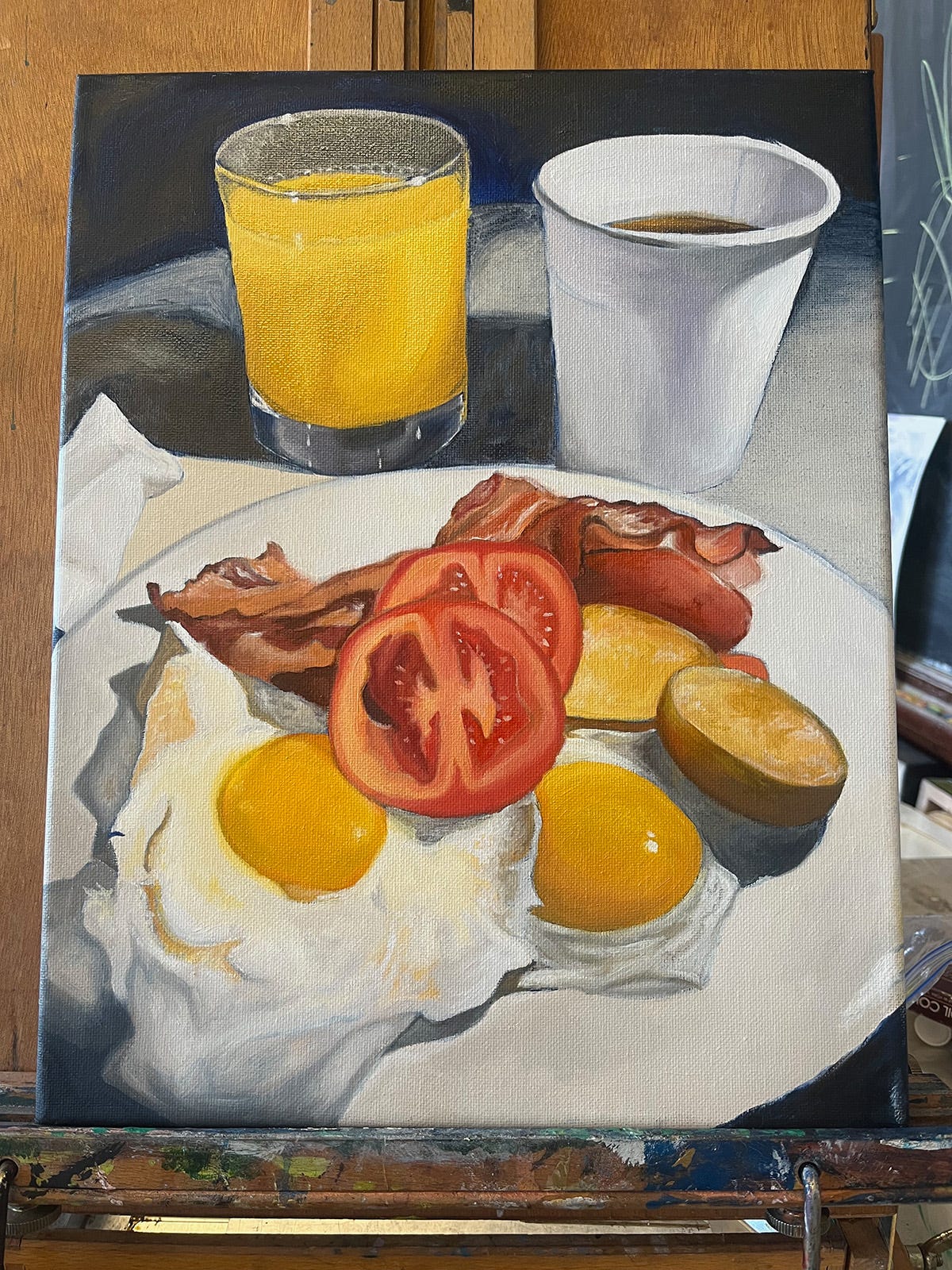 Unfinished painting of a dramatically lit breakfast of eggs, bacon and mini potatoes topped with two tomato slices. Behind the plate there's a glass of orange juice and a paper cup of coffee.