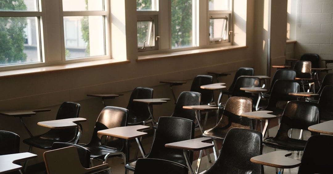 Empty classroom with desks and chairs by windows Empty classroom with desks and chairs by windows