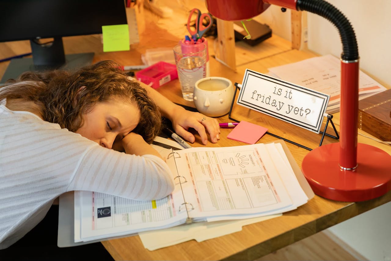 A tired women falls asleep with her head down on her desk under an orange lamp. A tired women falls asleep with her head down on her desk under an orange lamp.