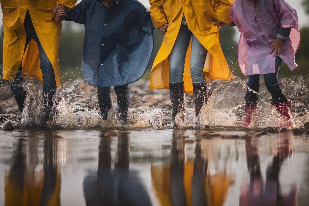 Waist-down shot of family in raincoats having fun while stepping into big puddle in nature.
