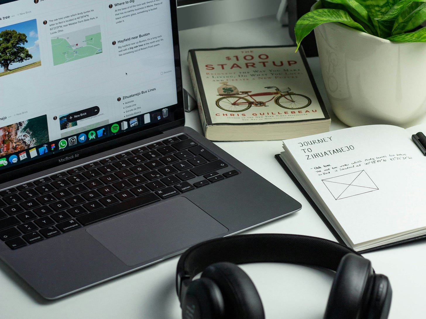A laptop, headphones, book and journal on a desk.