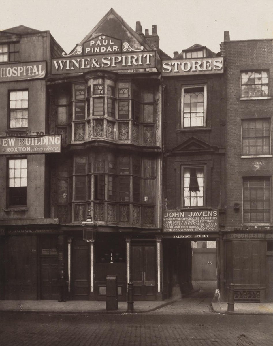 An old black and white photo of a building with a decoratively-carved wooden facade, with two buildings on either side of it An old black and white photo of a building with a decoratively-carved wooden facade, with two buildings on either side of it