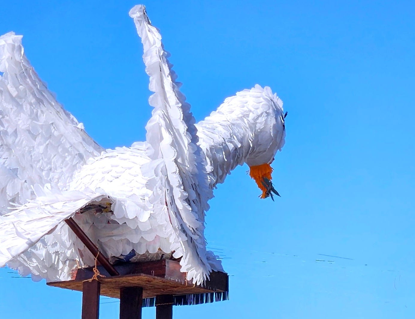 A papier machete dove riding on a platform in a truck (not shown), framed by bright blue sky A papier machete dove riding on a platform in a truck (not shown), framed by bright blue sky