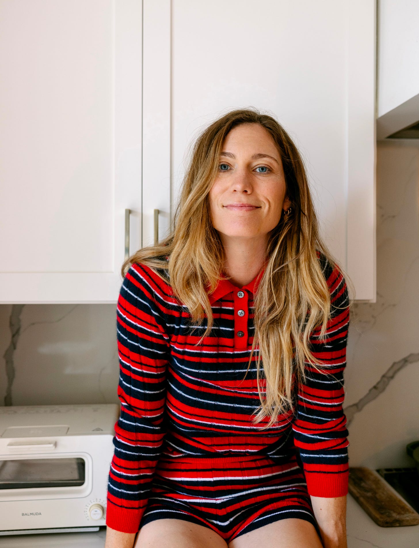 A photograph of nutritionist Mia Rigden in a striped matching set sitting on a countertop.