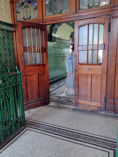 Metal turnstyle, pair of heavy wooden soors with stained glass windows, staircase with walls in tile