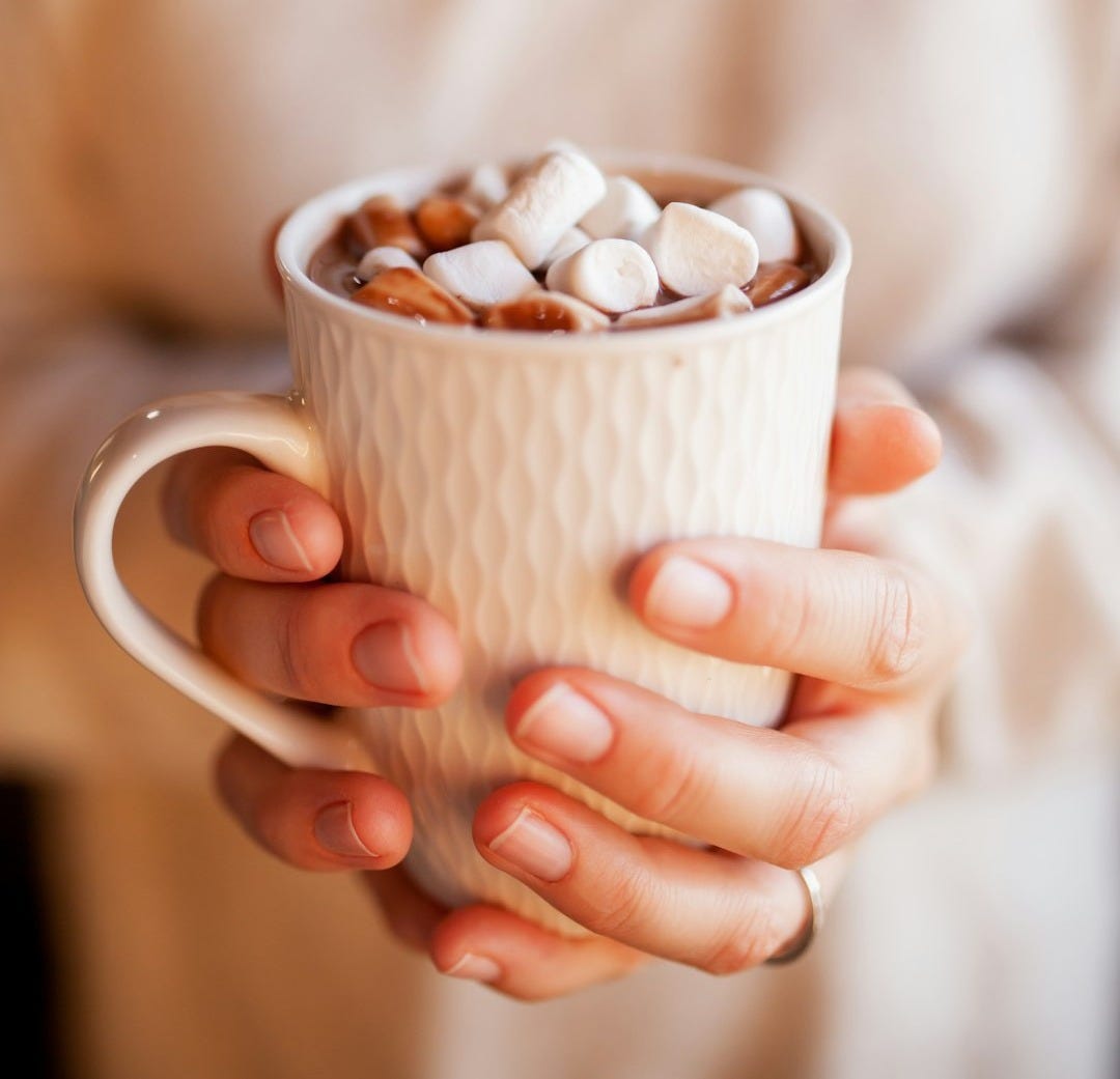 person holding white ceramic mug with brown and white beans