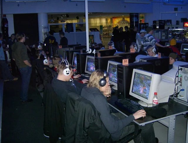 A 1990s internet café with rows of desktop computers in a cramped, shared room. A 1990s internet café with rows of desktop computers in a cramped, shared room.
