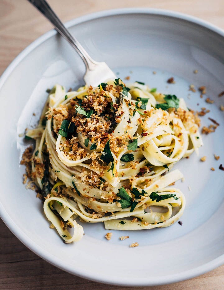 On the left, a plate of linguine with herbs and golden breadcrumbs, on the right, two bowls of green soup with cheese and chives alongside