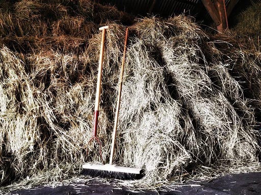 A pitchfork and broom leaning against bales of hay
