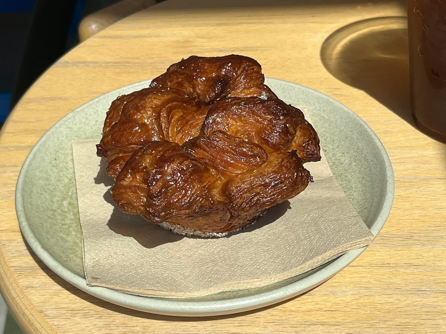 A round, laminated pastry with ridges that is well-browned on the outside, on a round, beige plate on a wooden table