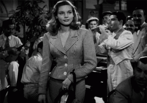 a woman in a plaid suit is standing in front of a crowd of people in a black and white photo .