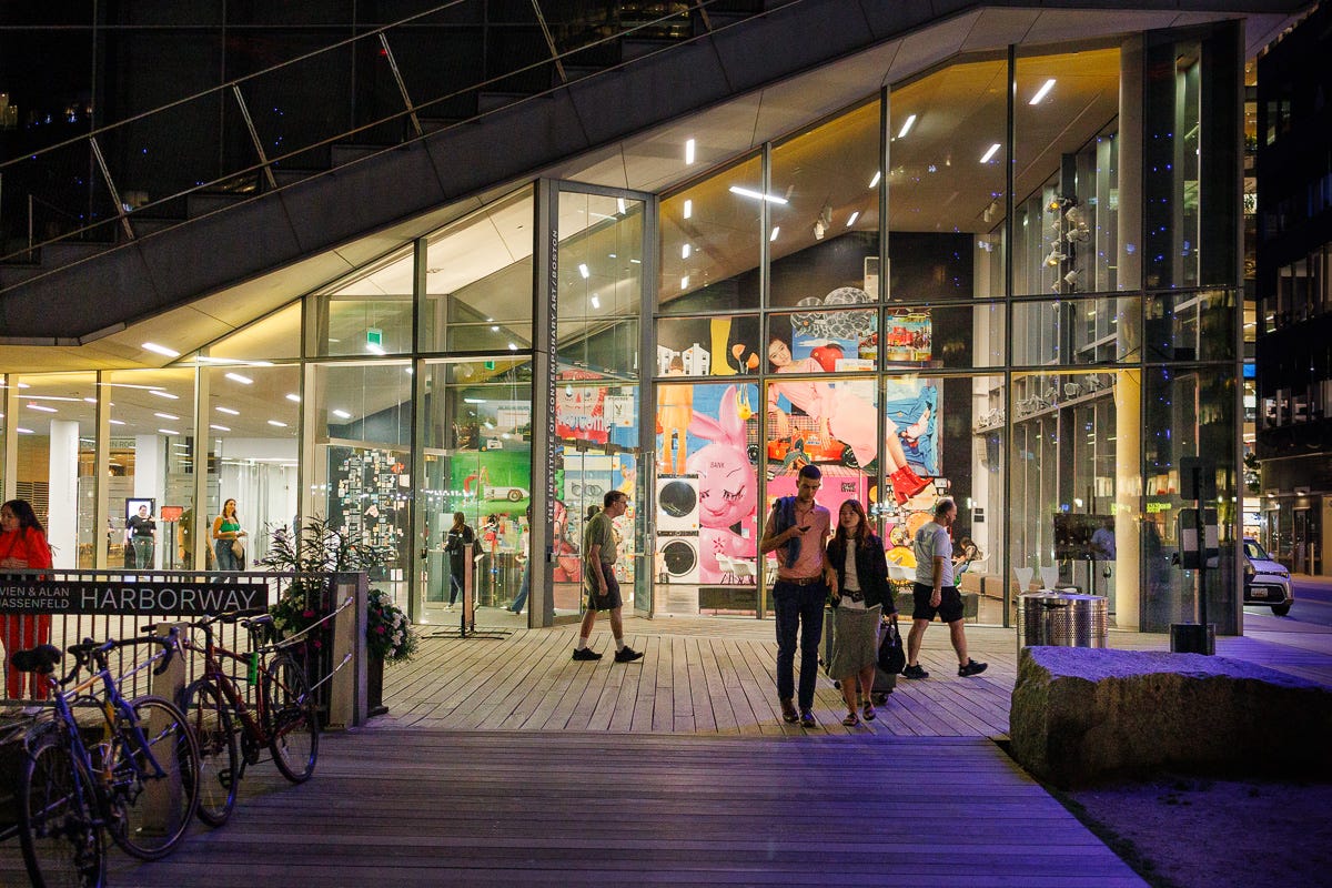 Institute of Contemporary Art glass building at night with colorful artwork visible inside and people walking outside